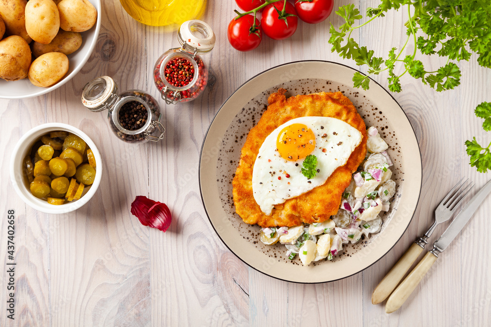 Viennese pork schnitzel with a fried egg. Served on potato salad. Natural wooden planks in the background. Viennese pork schnitzel with a fried egg. Served on potato salad. Natural wooden planks in the background.