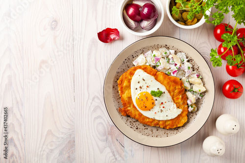 Viennese pork schnitzel with a fried egg. Served on potato salad. Natural wooden planks in the background.