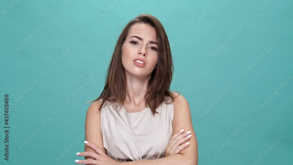 Displeased brunette woman in t-shirt showing thumb down and looking at the camera over turquoise background Displeased brunette woman in t-shirt showing thumb down and looking at the camera over turquoise background