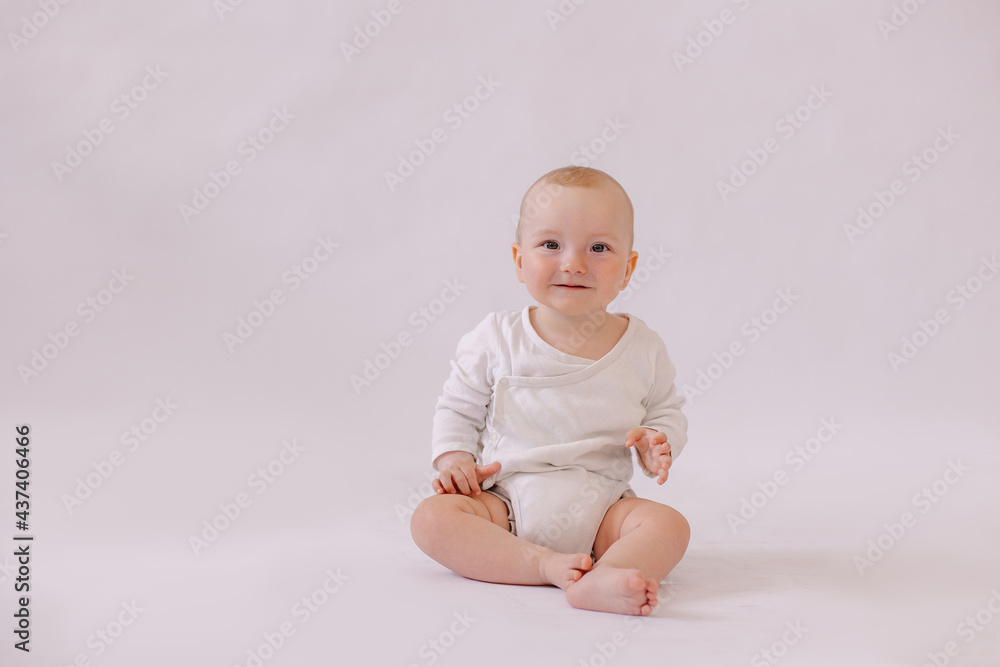 cute little kid in a white bodysuit sits on a white background. Copyspace. place for text. 8 months old boy smiling. looking at the camera. adorable child cute little kid in a white bodysuit sits on a white background. Copyspace. place for text. 8 months old boy smiling. looking at the camera. adorable child