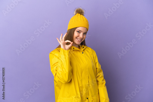 Teenager girl wearing a rainproof coat over isolated purple background showing ok sign with fingers