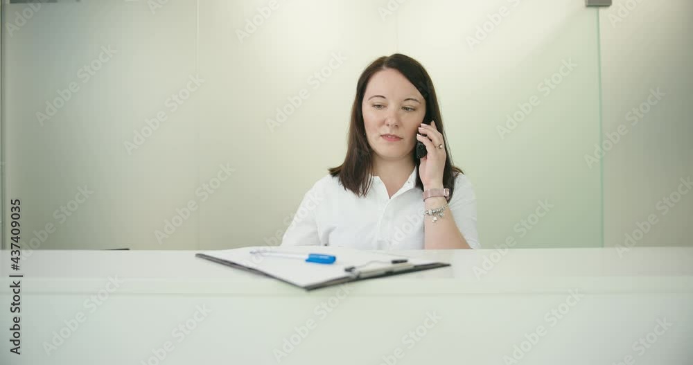 Animal vet clinic woman receptionist taking call and making notes looking at camera Animal vet clinic woman receptionist taking call and making notes looking at camera
