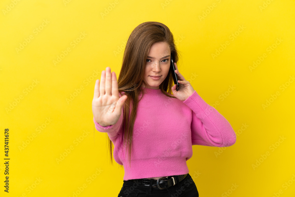 Teenager girl using mobile phone over isolated yellow background making stop gesture Teenager girl using mobile phone over isolated yellow background making stop gesture