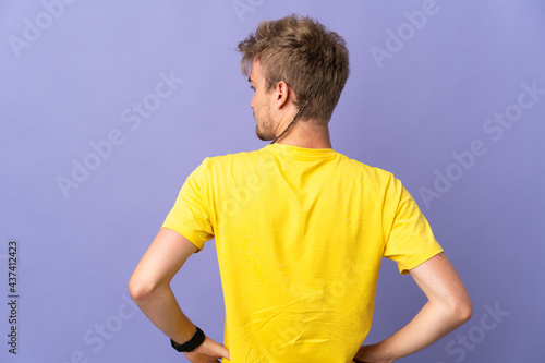 Young handsome blonde man isolated on purple background in back position and looking side