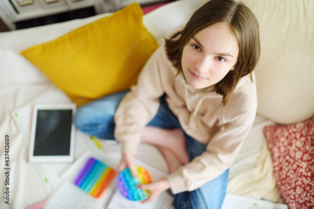 Teenage girl playing with rainbow pop-it fidget toy while studying at home. Teen kid with trendy stress and anxiety relief fidgeting game.