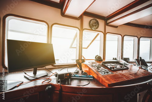 View of a cockpit area inside of a deckhouse of a modern safari or cruise yacht with a control panel on the wooden base and many navigation devices: compass, radio transceiver, radars, and dashboards photo