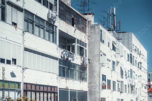 Multiple dwelling houses in a residential district of a European uptown with bright white buildings facades, balconies, dirt and rust, windows, drying laundry, roofs; sunny day, Lisbon, Portugal