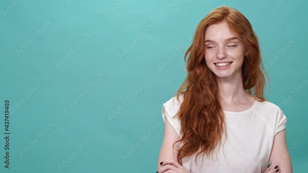 Happy ginger woman in t-shirt posing with crossed arms and pointing away over turquoise background Happy ginger woman in t-shirt posing with crossed arms and pointing away over turquoise background