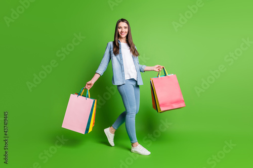 Full length body size view of attractive cheerful girl going holding bags new things isolated over bright green color background