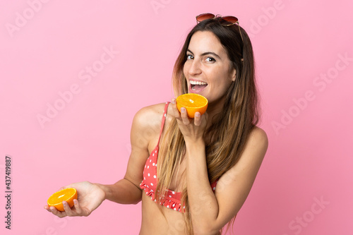 Young blonde woman over isolated pink background in swimsuit and holding an orange