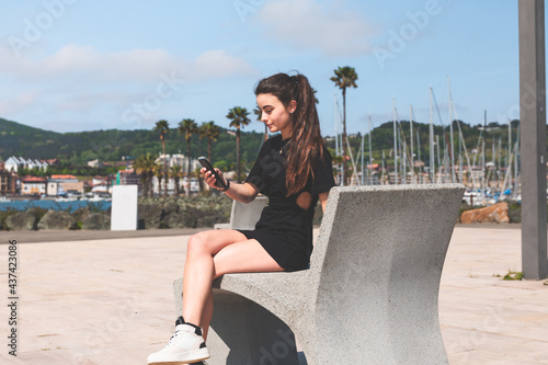 Young woman on a bench with a mobile phone at Hendaia, Basque Country.
