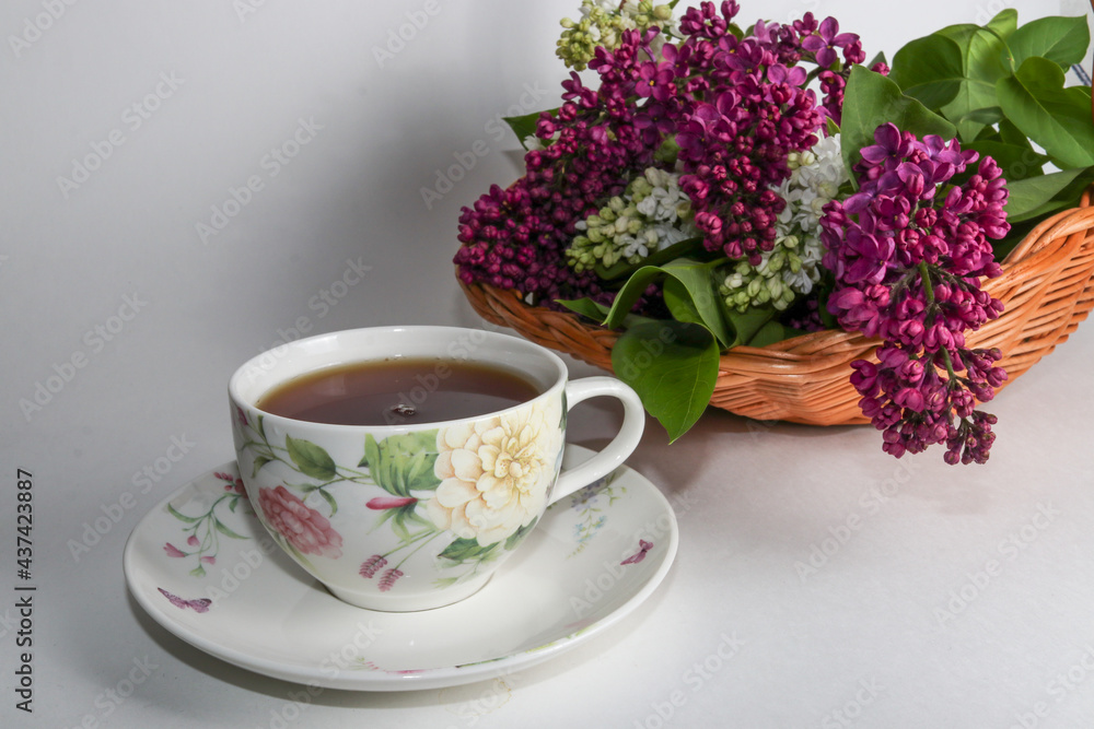 Branches of lilac and white lilac in a wicker basket and a cup of black tea with lilac flowers isolated on a white background Branches of lilac and white lilac in a wicker basket and a cup of black tea with lilac flowers isolated on a white background