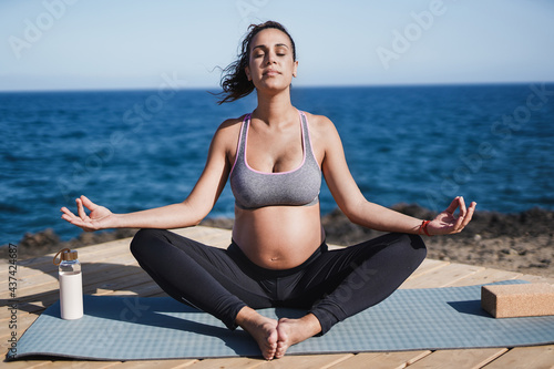Young pregnant woman doing yoga meditation on the beach - Maternity and healthy lifestyle concept
