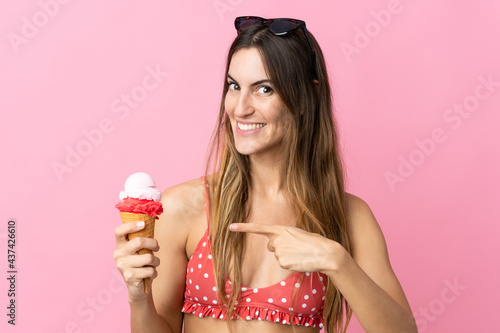 Young caucasian woman holding an ice cream isolated on pink background and pointing it