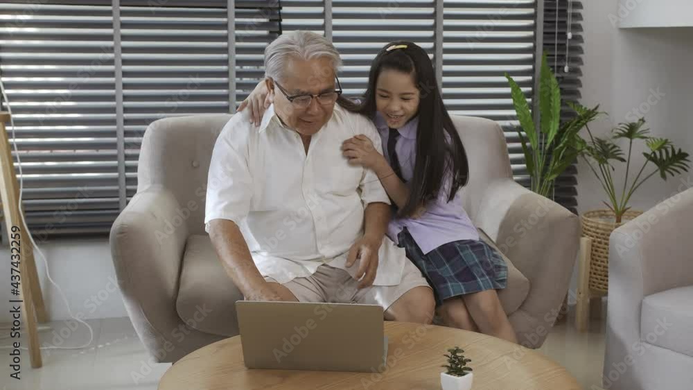 Senior Asian man and granddaughter on sofa chatting with friends via video call. Concept of new normal. Senior Asian man and granddaughter on sofa chatting with friends via video call. Concept of new normal.