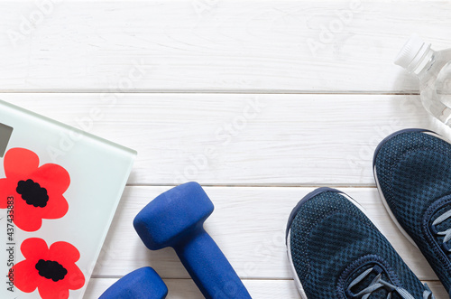 Sport oufit on the white wooden background, top view, copy space. Blue sneakers, blue dumbbells and white scales flatlay photo