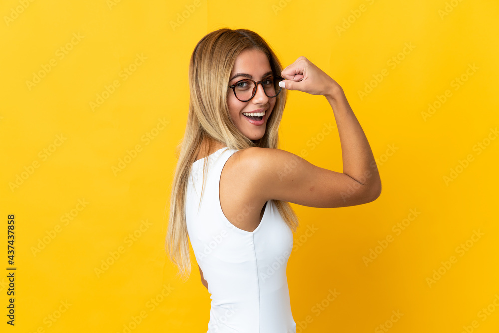 Young blonde woman isolated on yellow background doing strong gesture Young blonde woman isolated on yellow background doing strong gesture