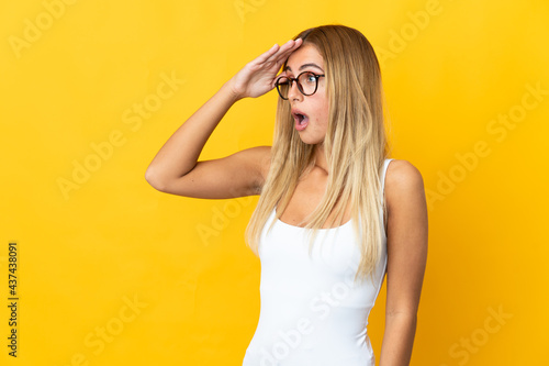 Young blonde woman isolated on yellow background with surprise expression while looking side