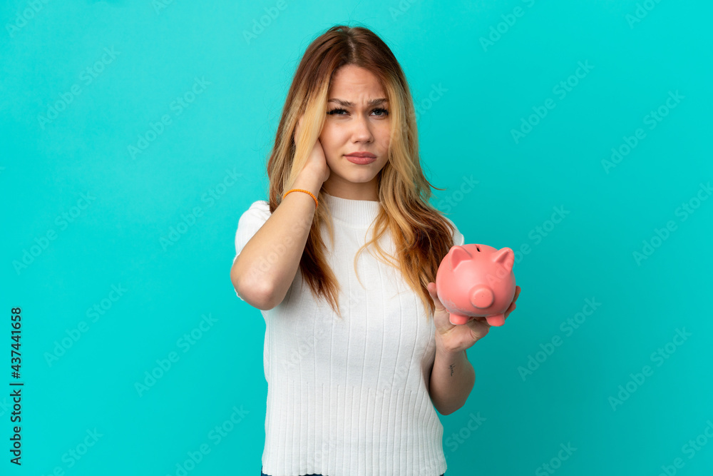 Teenager blonde girl holding a piggybank over isolated blue background frustrated and covering ears Teenager blonde girl holding a piggybank over isolated blue background frustrated and covering ears