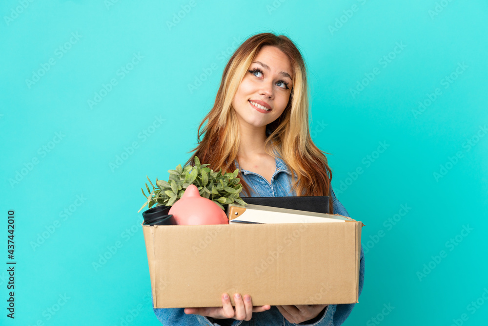 Teenager blonde girl making a move while picking up a box full of things thinking an idea while looking up Teenager blonde girl making a move while picking up a box full of things thinking an idea while looking up