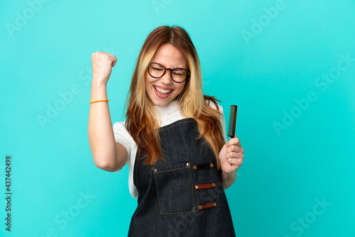 Young hairdresser girl over isolated blue background celebrating a victory