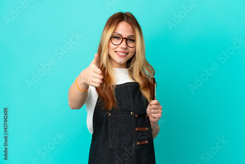 Young hairdresser girl over isolated blue background shaking hands for closing a good deal