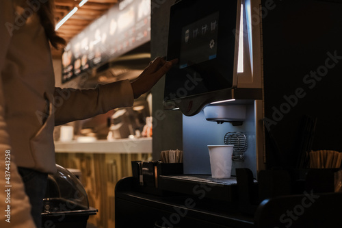 Obraz na plátně young woman prepares herself coffee through a self-service coffee machine in a cafe