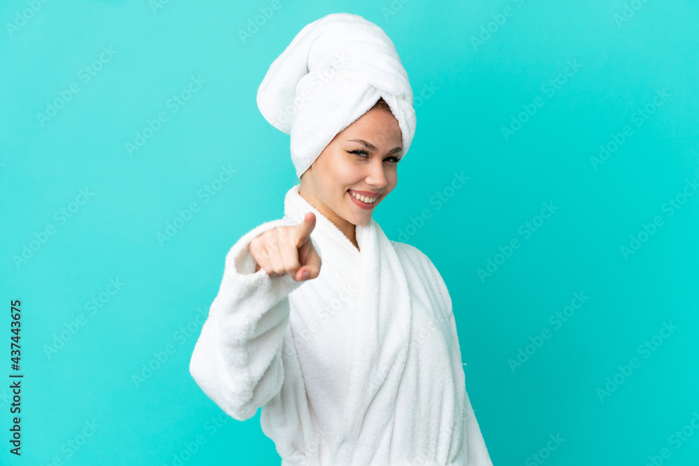 Teenager blonde girl in a bathrobe over isolated blue background pointing front with happy expression Teenager blonde girl in a bathrobe over isolated blue background pointing front with happy expression