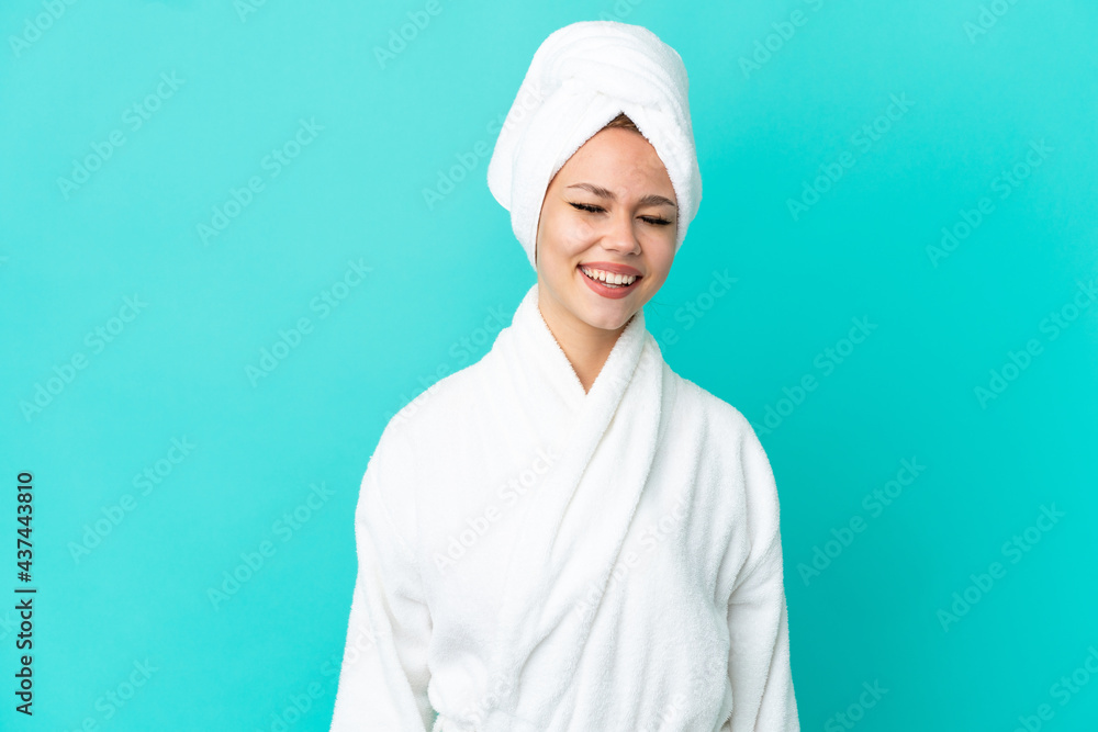 Teenager blonde girl in a bathrobe over isolated blue background laughing Teenager blonde girl in a bathrobe over isolated blue background laughing