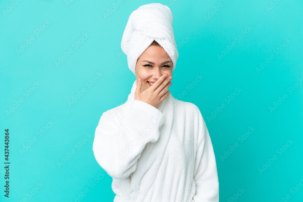Teenager blonde girl in a bathrobe over isolated blue background happy and smiling covering mouth with hand Teenager blonde girl in a bathrobe over isolated blue background happy and smiling covering mouth with hand