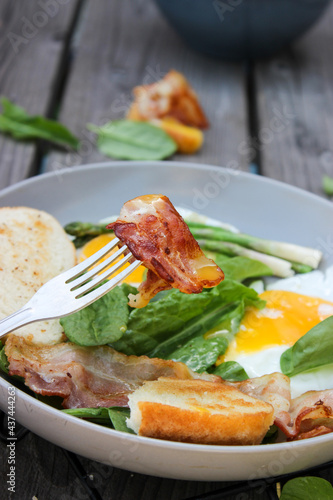 Breakfast on a plate of scrambled eggs with toasted bread, bacon and aromatic herbs