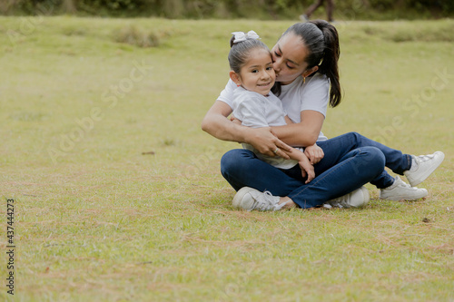 Wallpaper Mural Young Hispanic mom with her daughter sitting in the park-mother hugging and kissing her little daughter in the middle of the field outdoors Torontodigital.ca