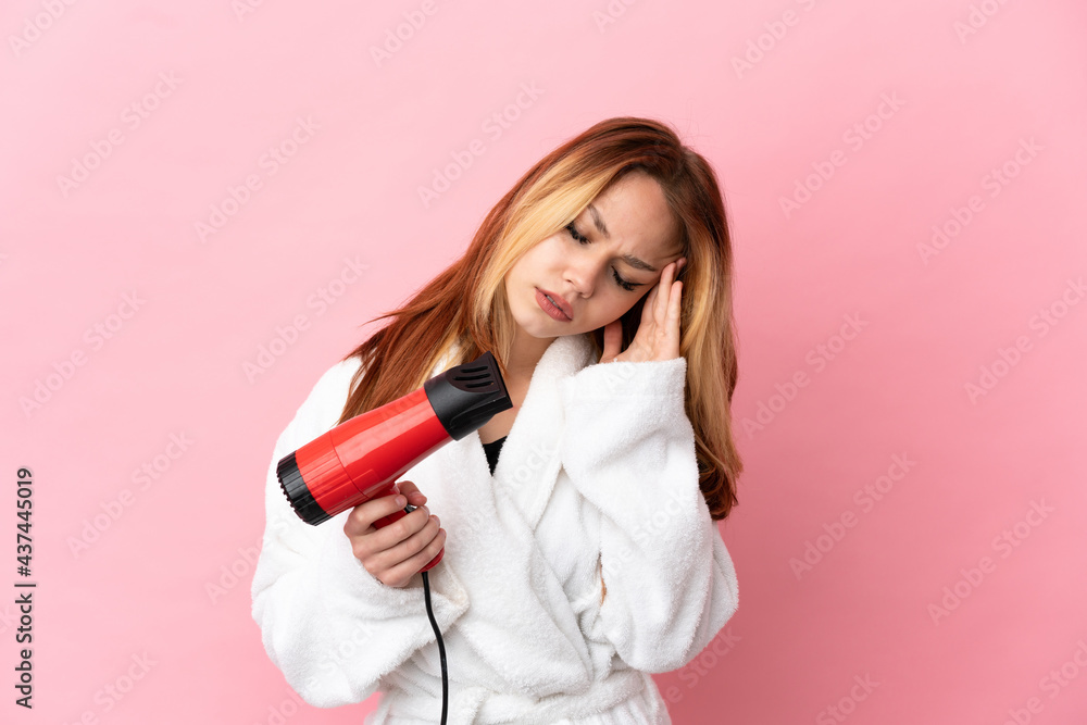 Teenager blonde girl holding a hairdryer over isolated pink background with headache Teenager blonde girl holding a hairdryer over isolated pink background with headache