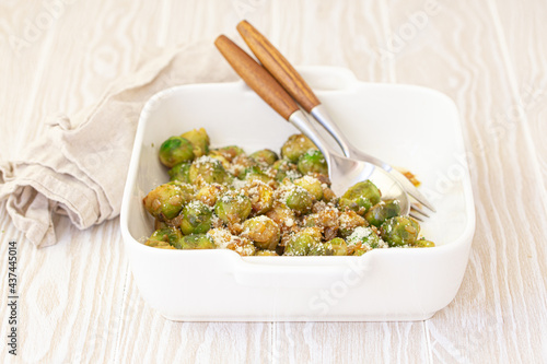 Healthy vegetarian dish roasted brussels sprouts with butter and parmesan cheese in white ceramic casserole close up on wooden table angle view, vegan food 