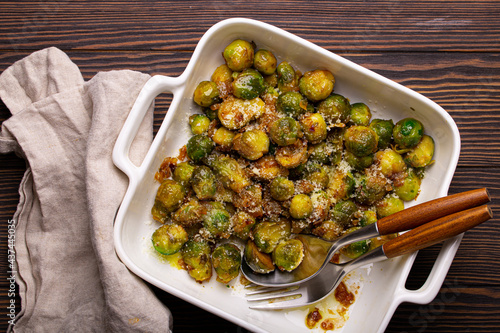 Healthy vegetarian dish roasted brussels sprouts with butter and parmesan cheese in white ceramic casserole top view on dark rustic wooden table from above, vegan food 