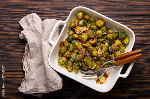 Healthy vegetarian dish roasted brussels sprouts with butter and parmesan cheese in white ceramic casserole top view on dark rustic wooden table from above, vegan food   photo