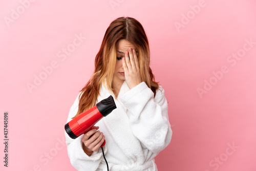 Teenager blonde girl holding a hairdryer over isolated pink background with tired and sick expression