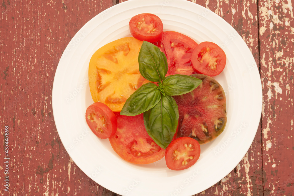 Variety of freshly picked and sliced tomatoes with sprig of basil on a white plate