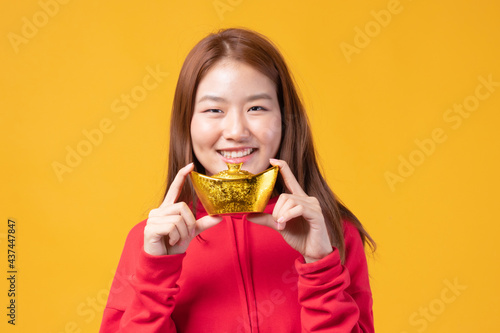 Beautiful Asian woman holding gold ingot that Represents wealth and prosperity isolated on yellow background. Happy Chinese new year concept.