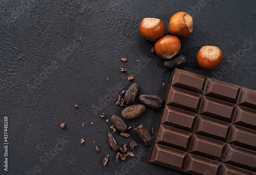 Close-up of a chocolate bar with nuts and cocoa beans on a dark stone background.