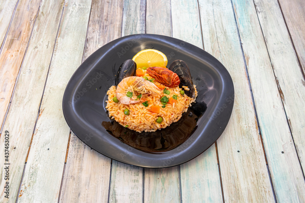 Delicious Peruvian dish of rice with seafood. River crab, carrot, peas, parsley, prawns, mussels, clams and lemon in black plate Delicious Peruvian dish of rice with seafood. River crab, carrot, peas, parsley, prawns, mussels, clams and lemon in black plate