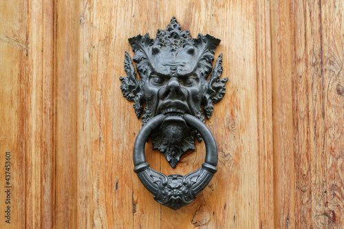 Tableau sur toile Old metal door knocker with satyrs head on a wooden door, Florence, Italy