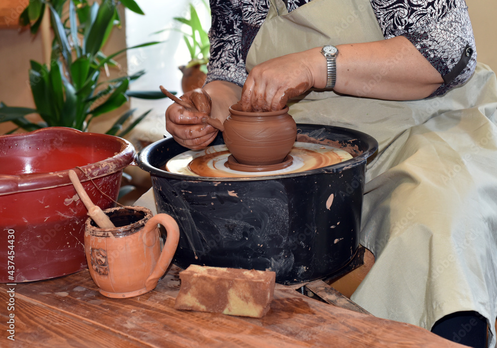 A female potter shows a master class on making a clay pot on a potter's wheel. A female potter shows a master class on making a clay pot on a potter's wheel.
