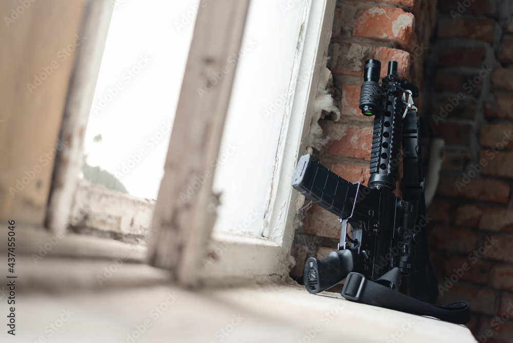 Black airsoft rifle with collimator sight on the window sill close up ...