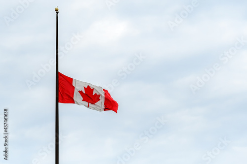 A Canadian flag at half mast, lowered in remembrance of the indigenous children who were abused and dies in residential schools. Overcast, wide view. photo