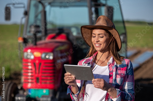 Female agronomist standing in field in front of tractor using tablet
