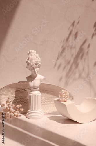 Vintage interior composition with sunlight and shadows in minimalist style. Geometric shapes, plate, plaster girl and gypsophila flowers on a light beige background. 