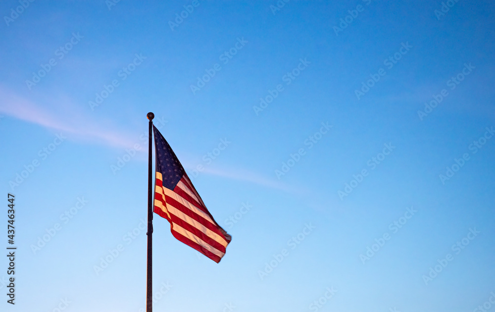 The American flag flies under blue skies as the sun goes down.