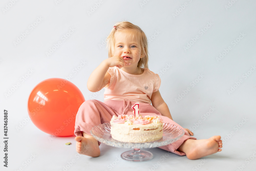 little beautiful blue-eyed girl celebrates her first birthday in the style smash a cake and she tastes her first birthday cake on a blue background with balloons little beautiful blue-eyed girl celebrates her first birthday in the style smash a cake and she tastes her first birthday cake on a blue background with balloons