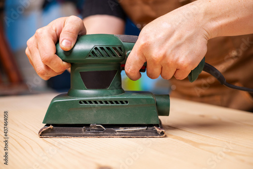 Closeup of carpenter sanding wooden planks with electrical sanding machine. A carpenter grinds wood with sander machine photo